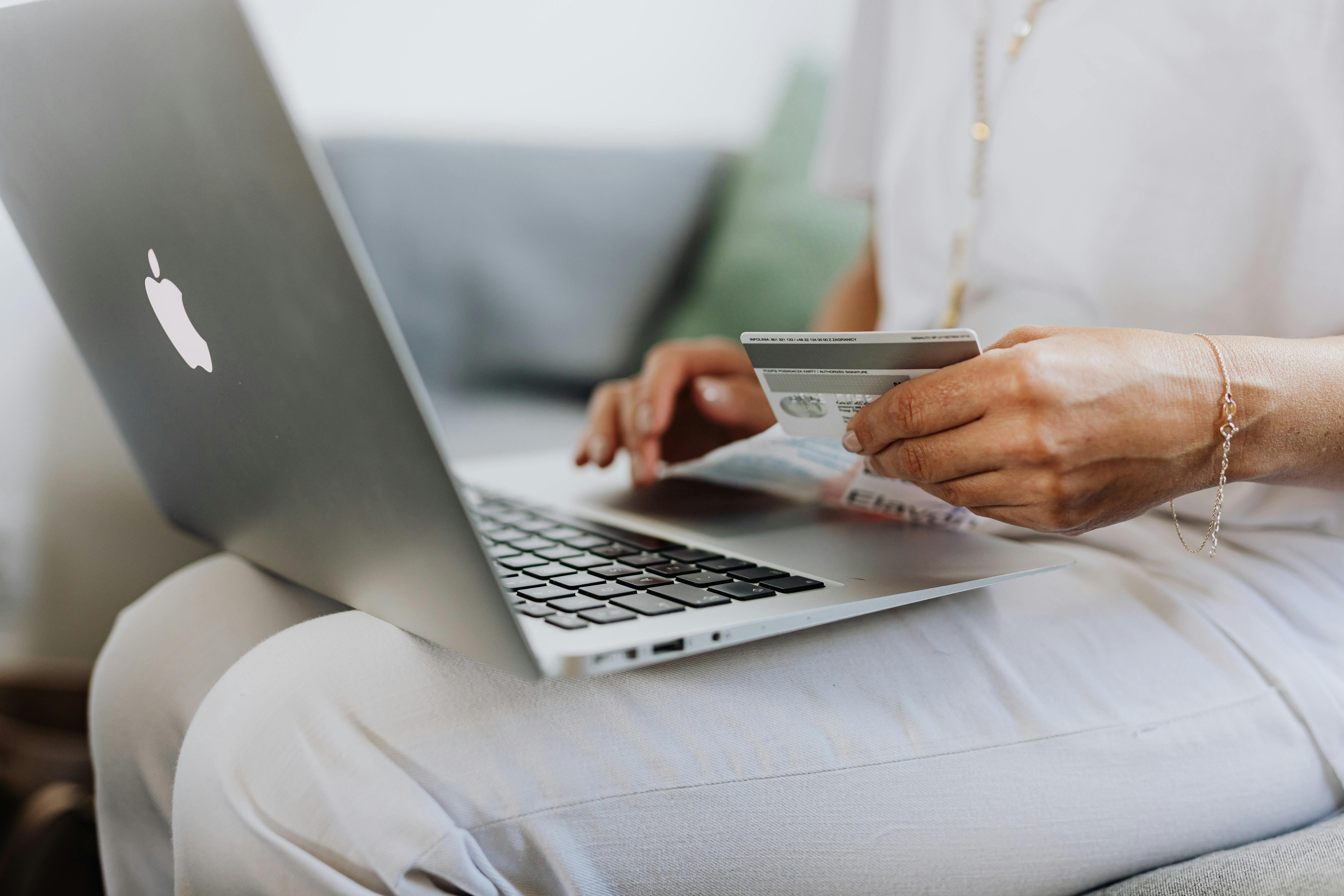 A person's hands hold a credit card and type on a silver laptop computer.